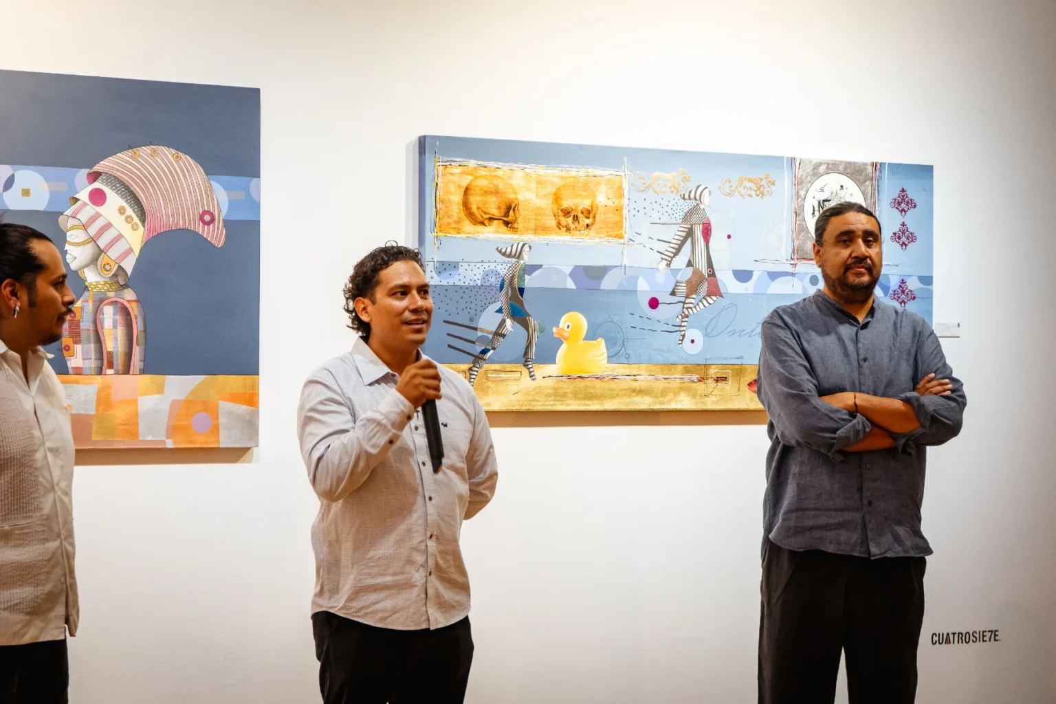 Director de galería hablando en inauguración dentro de Cuatrosie7e Galería en Oaxaca frente a obra contemporánea.